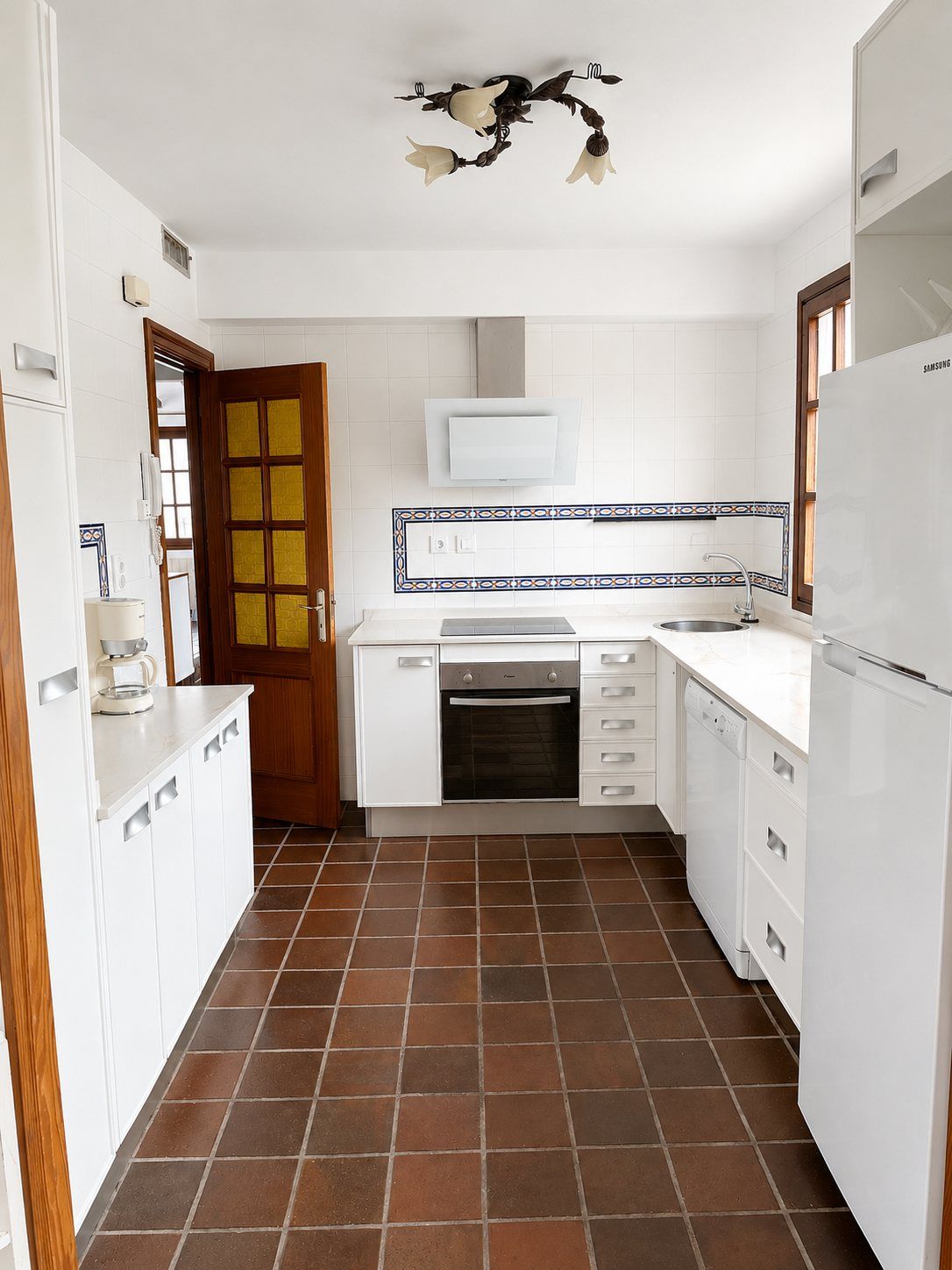 La cocina blanca de pasillo, con suelo de baldosa de terracota.