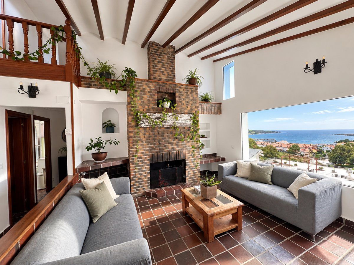 Un salón de techos altos con chimenea de ladrillo, dos sofás y un amplio ventanal con vistas al mar.