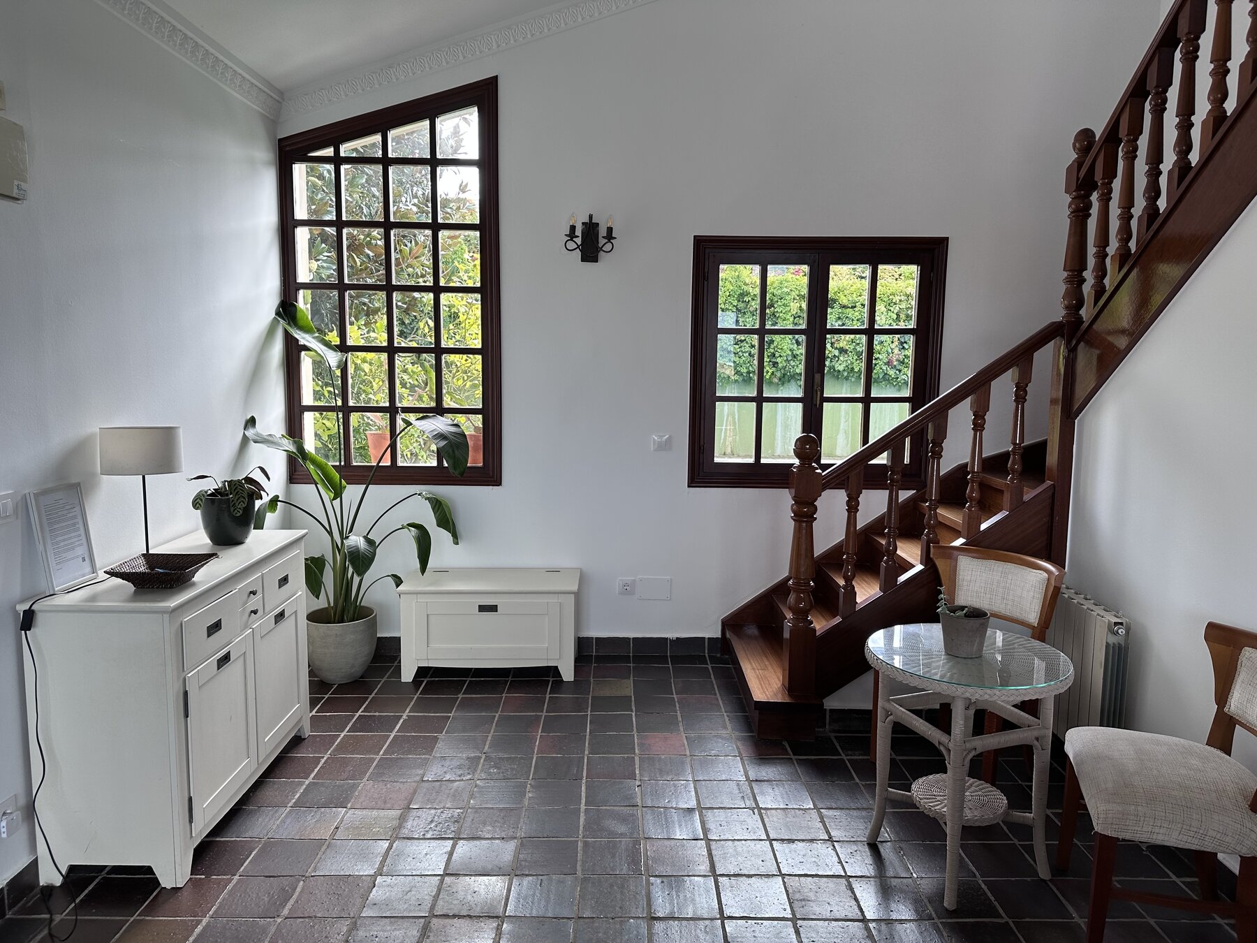 A bright entry room with tall windows, potted plants and a wooden staircase.